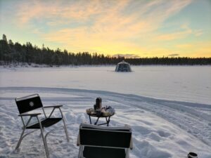 All about Swedish Lapland in winter. Beautiful scenery outside our igloo. In the foreground there is one camping table with two small chairs and breakfast upon the table. On background another glass igloo.