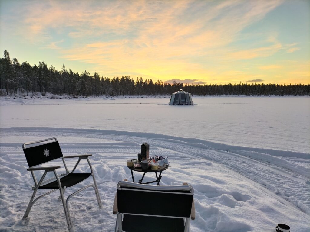 All about Swedish Lapland in winter. Beautiful scenery outside our igloo. In the foreground there is one camping table with two small chairs and breakfast upon the table. On background another glass igloo.